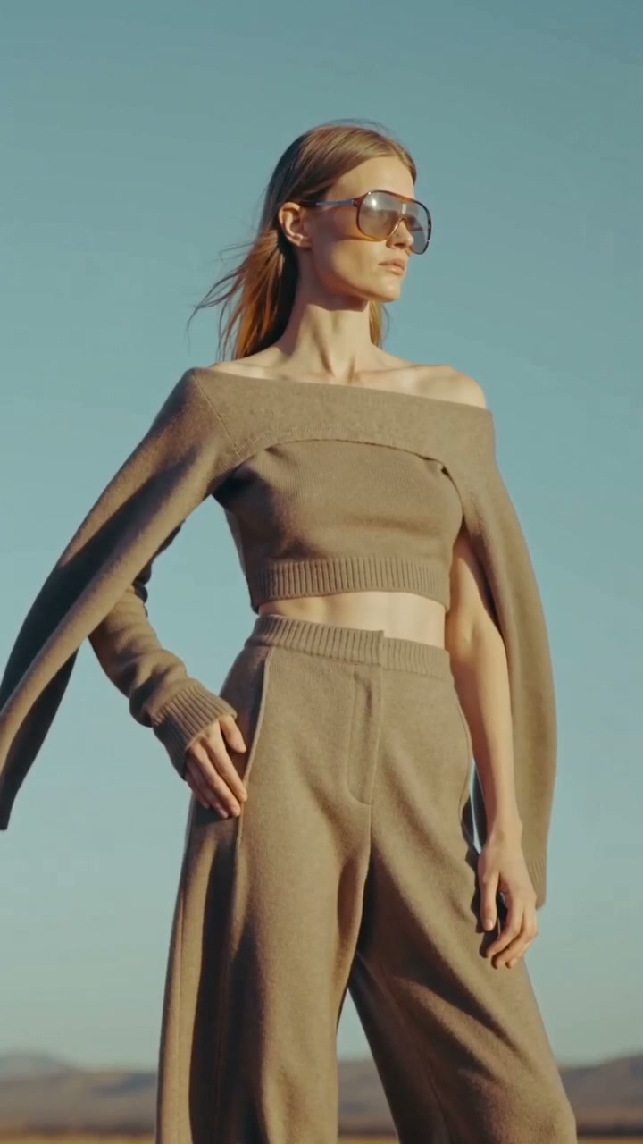 Woman in sunglasses wearing taupe knitwear against a blue sky